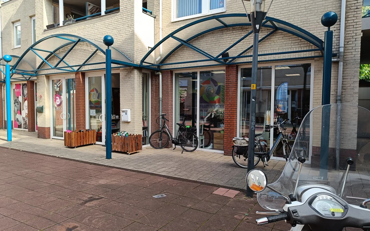 Winkelfront met glazen afdak, houten deuren en ingang, fietsen geparkeerd ervoor