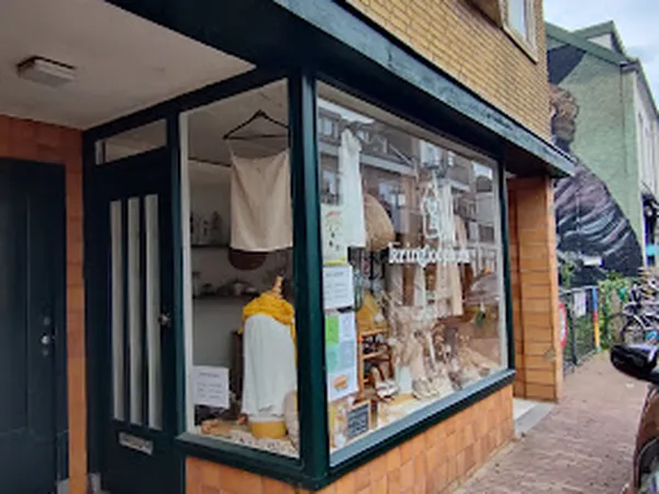 Winkelruit met etalage van kringloopwinkel, donkergroene pui met uitgestalde kleding op mannequins