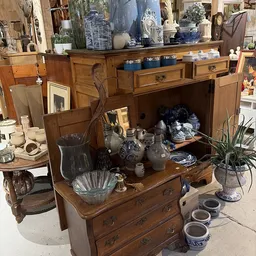 Houten kast met open deuren vol diverse tweedehands huishoudartikelen, servies en decoratie