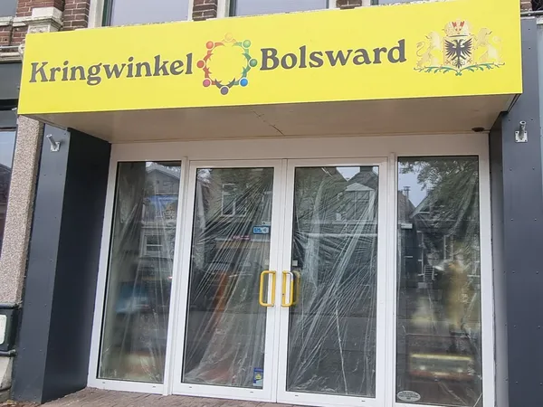 Gevel van kringloopwinkel met geel uithangbord en glazen deuren