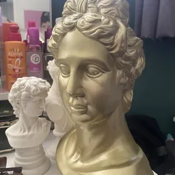 Goudkleurig decoratief busthoofd met klassieke sculptuurstijl, met kleinere witte replica ernaast