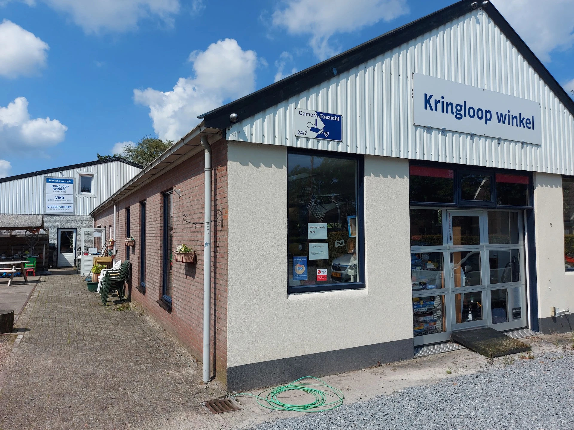 Voorgevel van Kringloop winkel Bovensmilde met bakstenen zijvleugel en wit winkelfront met blauwe deuren