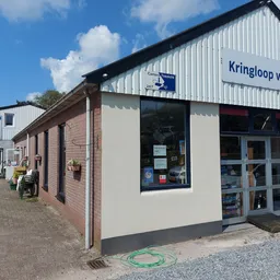 Voorgevel van Kringloop winkel Bovensmilde met bakstenen zijvleugel en wit winkelfront met blauwe deuren