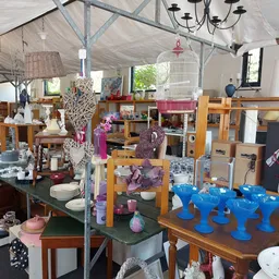 Winkelbinnenruimte met veel uitgestalde spullen op tafels en stellingen, waaronder servies, decoraties en meubelen.