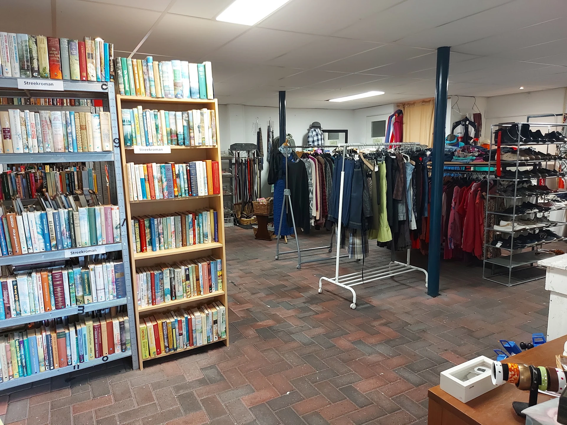 Winkelinterieur met boekenrekken links en kledingrekken met jassen rechts