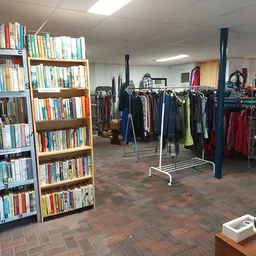 Winkelinterieur met boekenrekken links en kledingrekken met jassen rechts