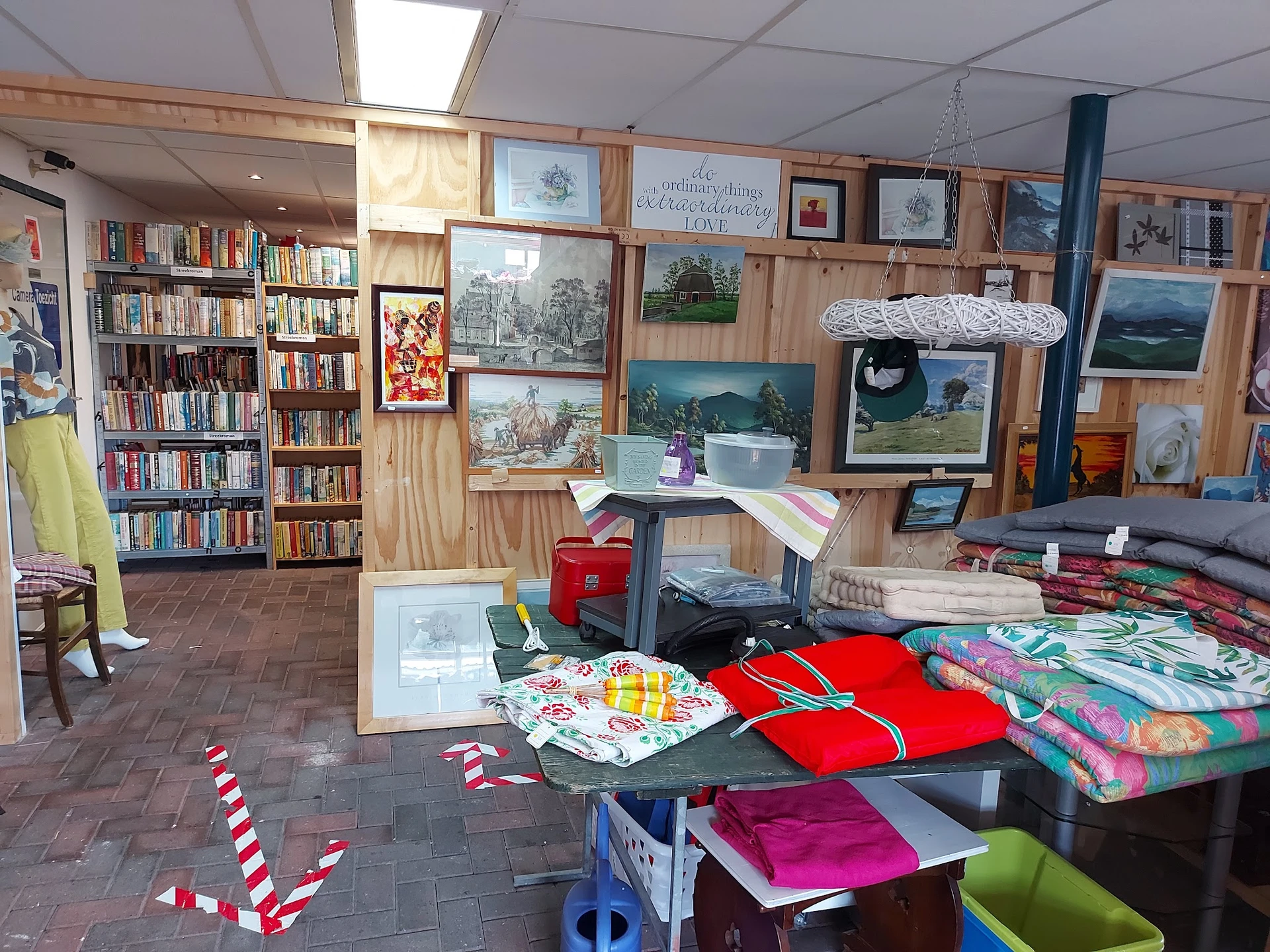 Winkelbinnenruimte met boekenkasten, kunstwerken aan muur, textielwaren en huishoudartikelen op tafels