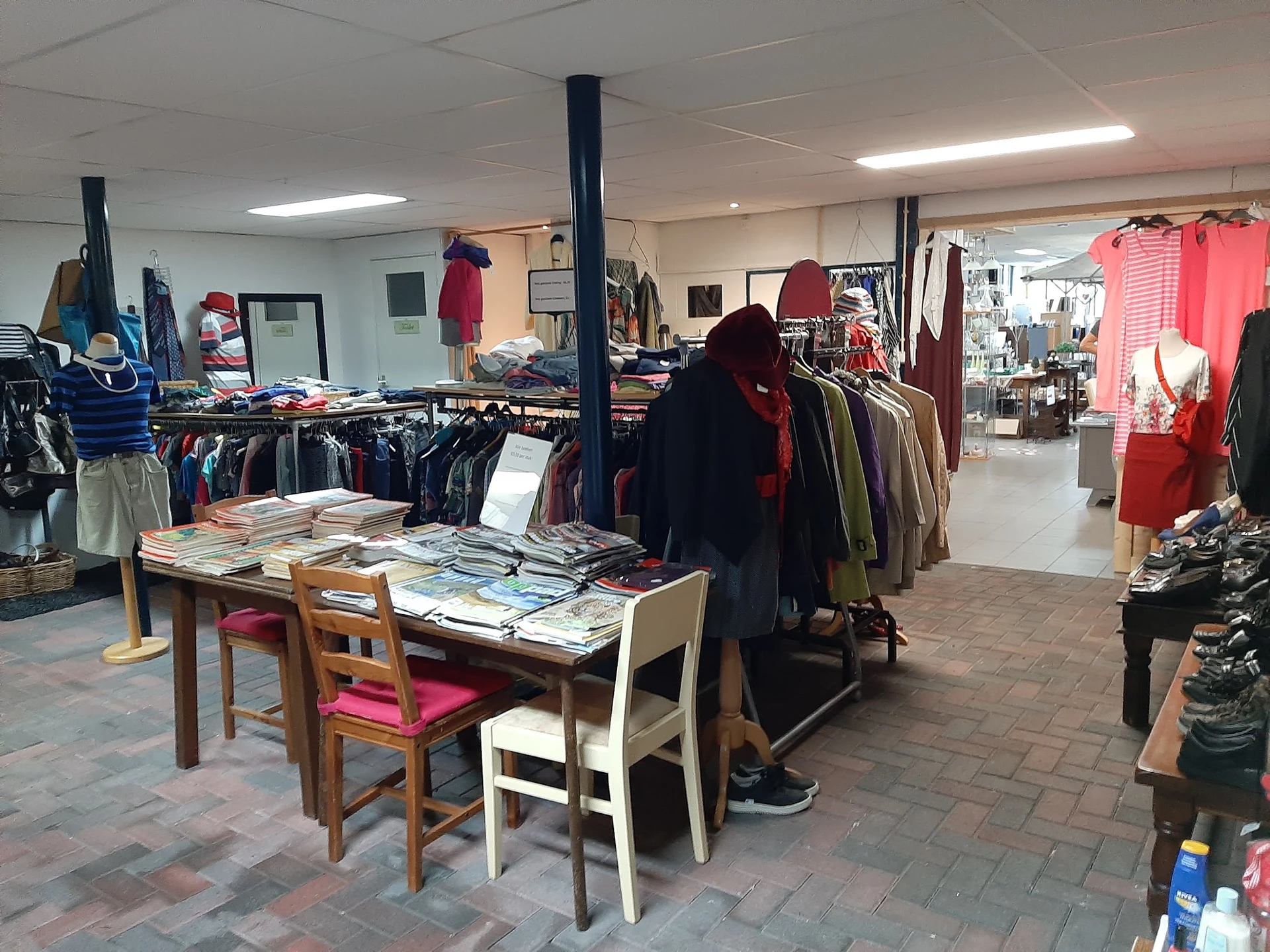 Winkelvloer met kledingrekken, tafel met uitgelegde spullen en personeel aan het werk in de kringloopwinkel