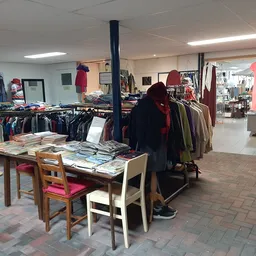 Winkelvloer met kledingrekken, tafel met uitgelegde spullen en personeel aan het werk in de kringloopwinkel