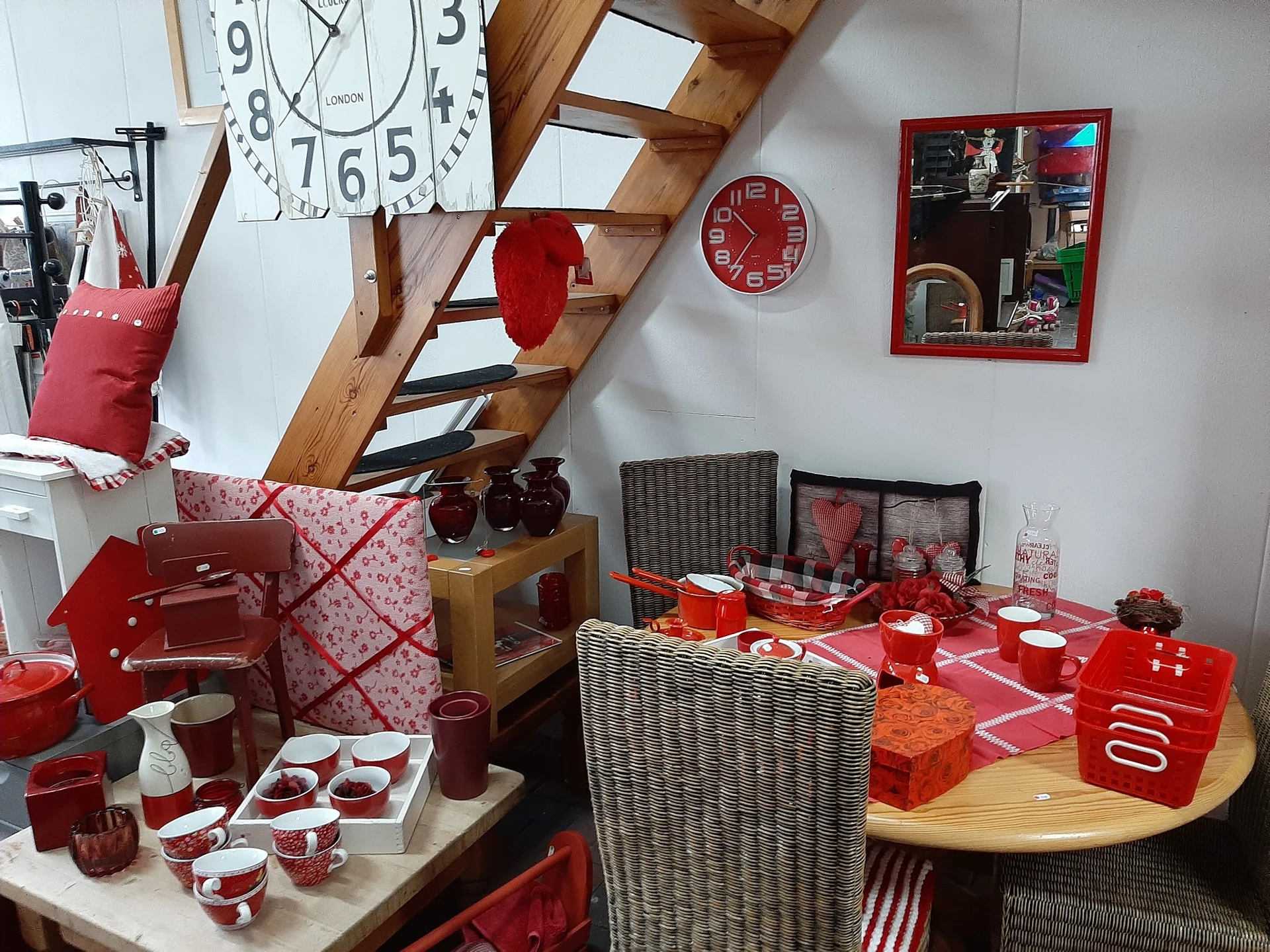 Uitgestalde rode huishoudartikelen en accessoires in de winkel, waaronder servies, pannen, kopjes en decoratieve items op taf