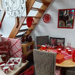 Uitgestalde rode huishoudartikelen en accessoires in de winkel, waaronder servies, pannen, kopjes en decoratieve items op taf