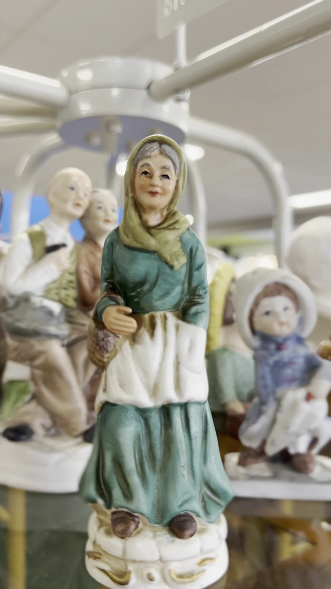 Verzameling van beeldjes en figuren, waaronder een vrouwenbeeldje in groen en wit met hoofddoek op de voorgrond
