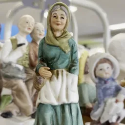 Verzameling van beeldjes en figuren, waaronder een vrouwenbeeldje in groen en wit met hoofddoek op de voorgrond