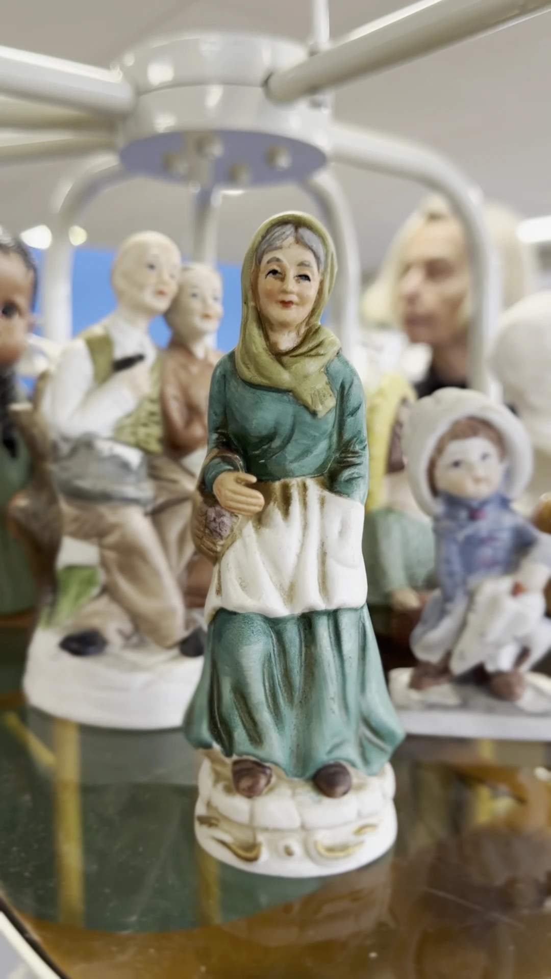 Verzameling vintage beeldjes en figuren, waaronder een vrouw in groen en wit kleed met hoofddoek in close-up op de voorgrond