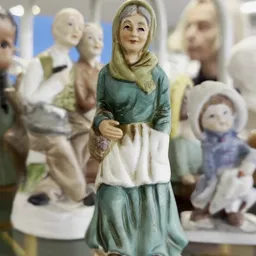 Verzameling vintage beeldjes en figuren, waaronder een vrouw in groen en wit kleed met hoofddoek in close-up op de voorgrond