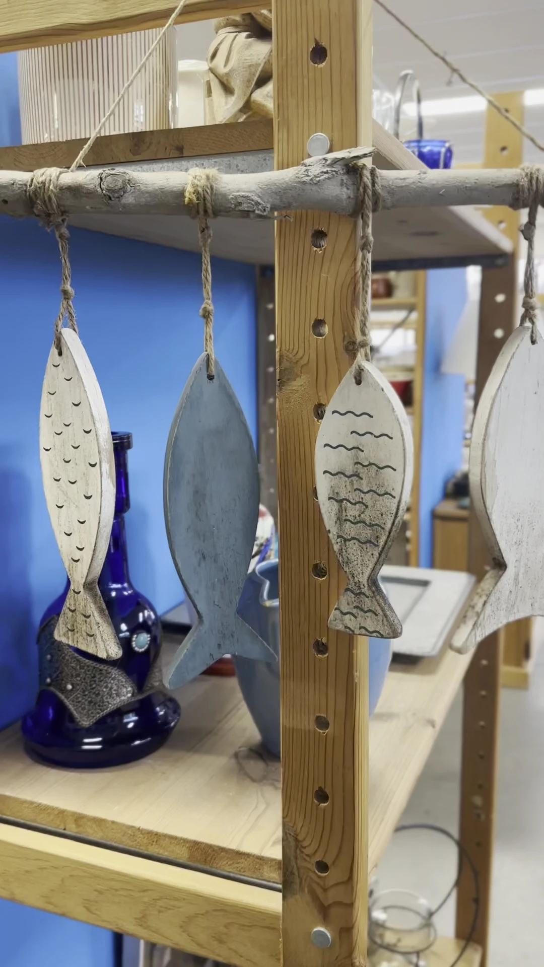 Vier decoratieve houten vissen aan touw, hangend tegen blauwe wand en houten wand