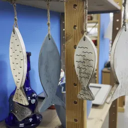 Vier decoratieve houten vissen aan touw, hangend tegen blauwe wand en houten wand