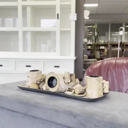 Decoratieve tafelschikking met witte stenen objecten en vazen op zwarte plateau