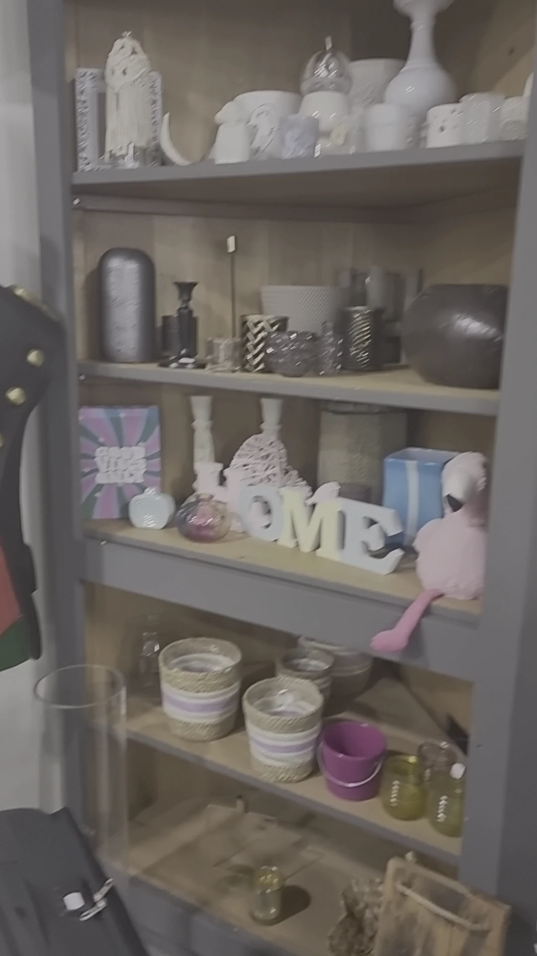 Opzet van decoratieve items op een plank met witte letters, vazen, roze figuren en diverse huishoudartikelen