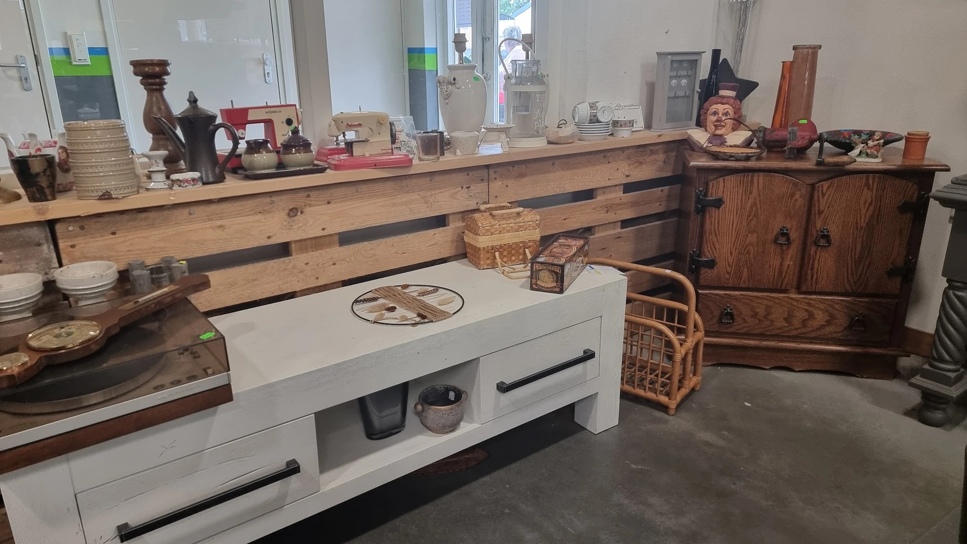 Winkelvloer met houten toonbank, witte kast, vintage spullen en houten meubels langs de muur