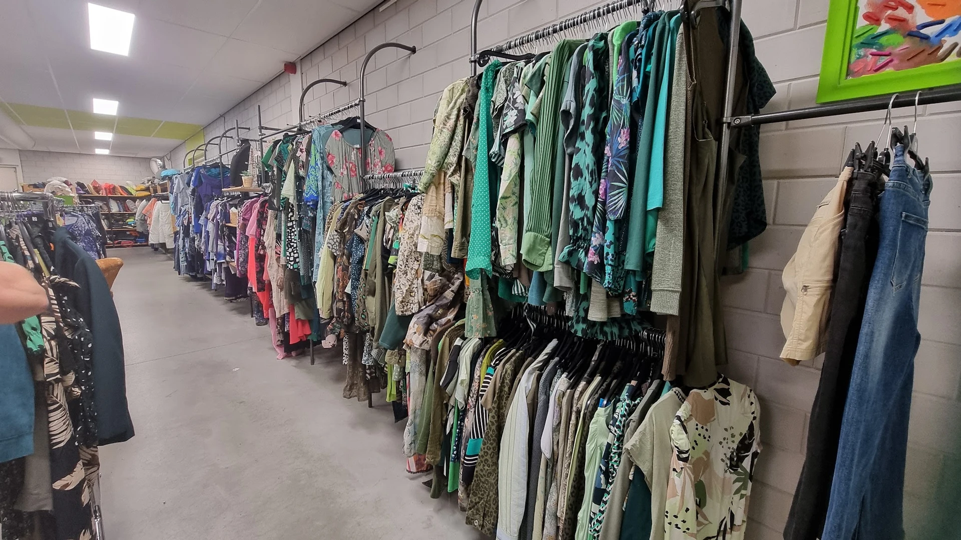 Lange rijen kledingrekken met tweedehands kleding in verschillende kleuren en stijlen
