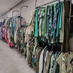 Lange rijen kledingrekken met tweedehands kleding in verschillende kleuren en stijlen