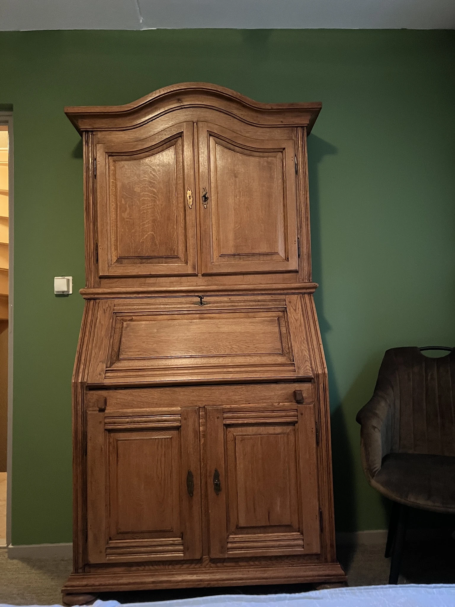 Houten secretaire met twee deuren bovenaan en uitgeklapt schrijfblad, tegen groene muur