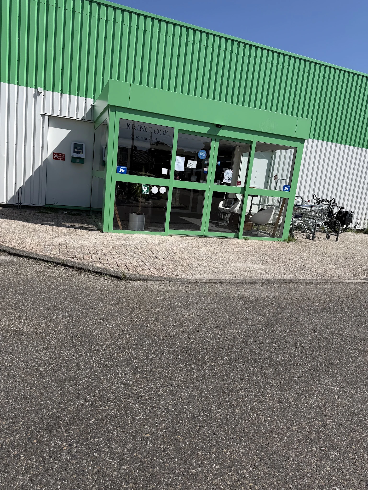 Groene winkelgevel met glazen deuren en ramen, fietsen geparkeerd ervoor op plaveisel