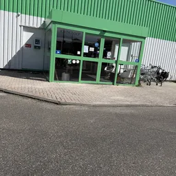 Groene winkelgevel met glazen deuren en ramen, fietsen geparkeerd ervoor op plaveisel