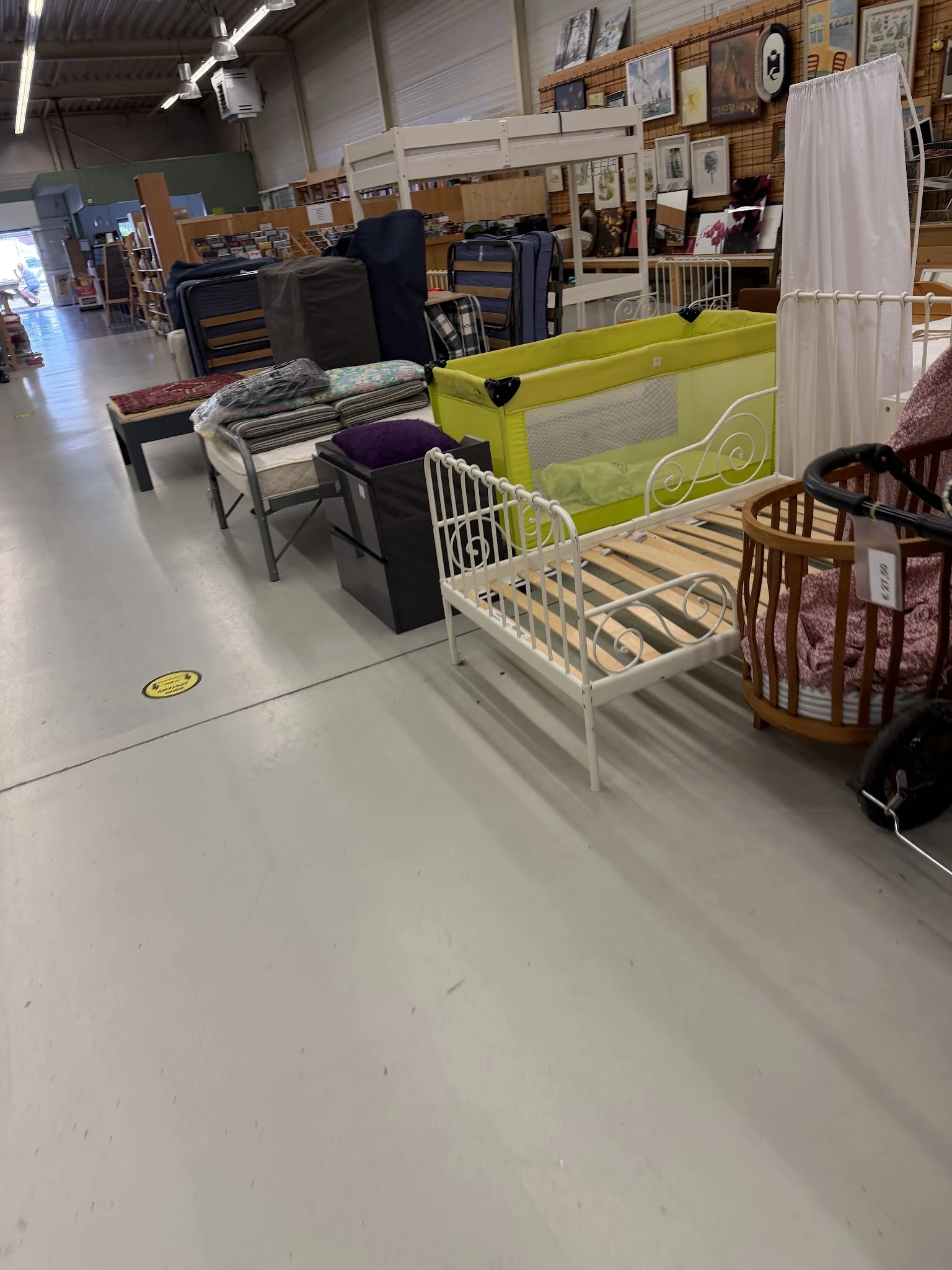 Uitgestalde kindermeubels in de winkel: wit kinderbed, groene babybox en houten wiegjes