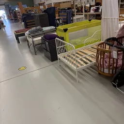 Uitgestalde kindermeubels in de winkel: wit kinderbed, groene babybox en houten wiegjes