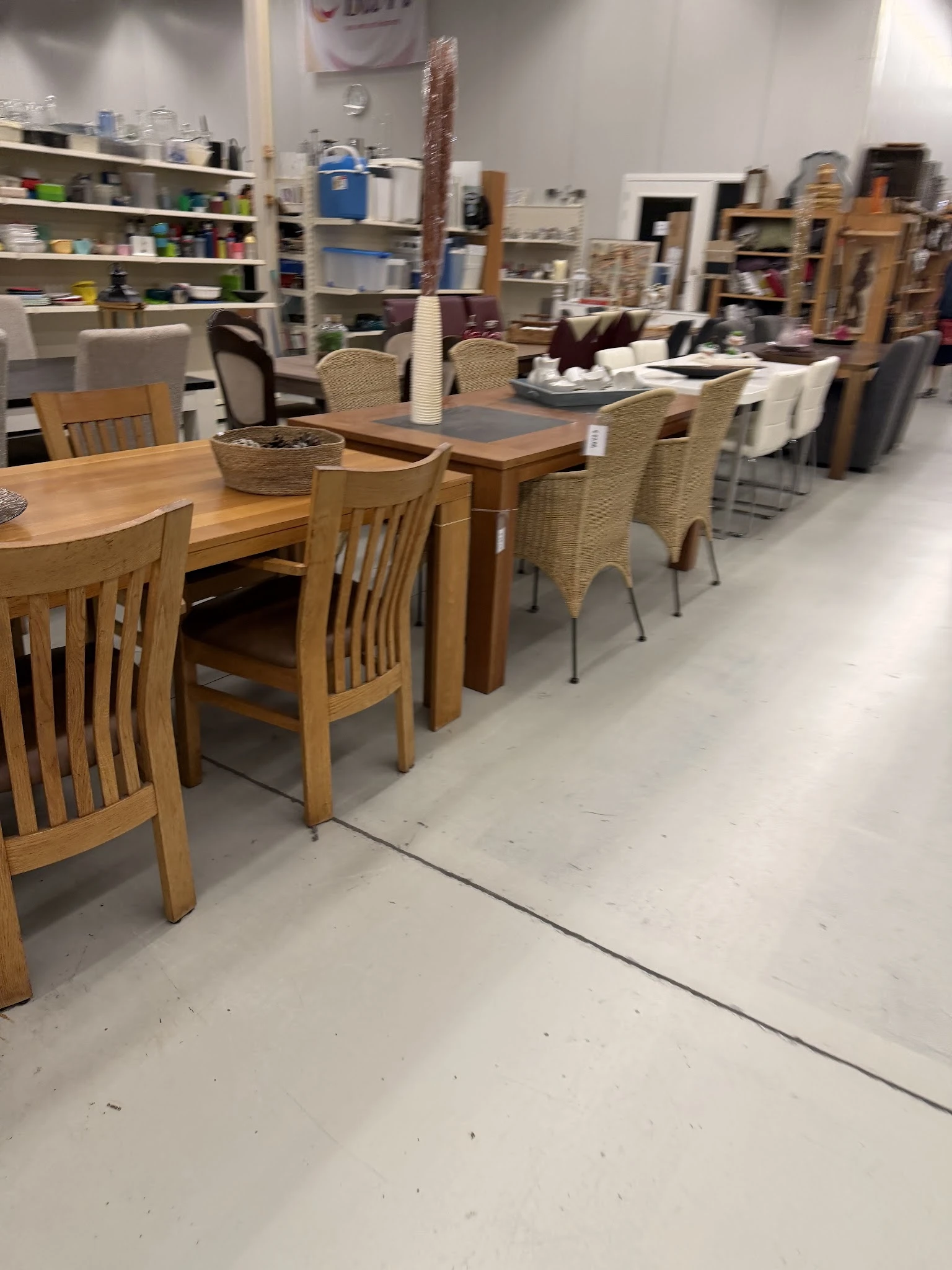 Uitgestalde eet- en zitmeubels: houten eettafels met stoelen en rieten stoelen in een kringloopwinkel