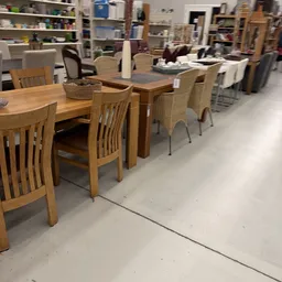 Uitgestalde eet- en zitmeubels: houten eettafels met stoelen en rieten stoelen in een kringloopwinkel