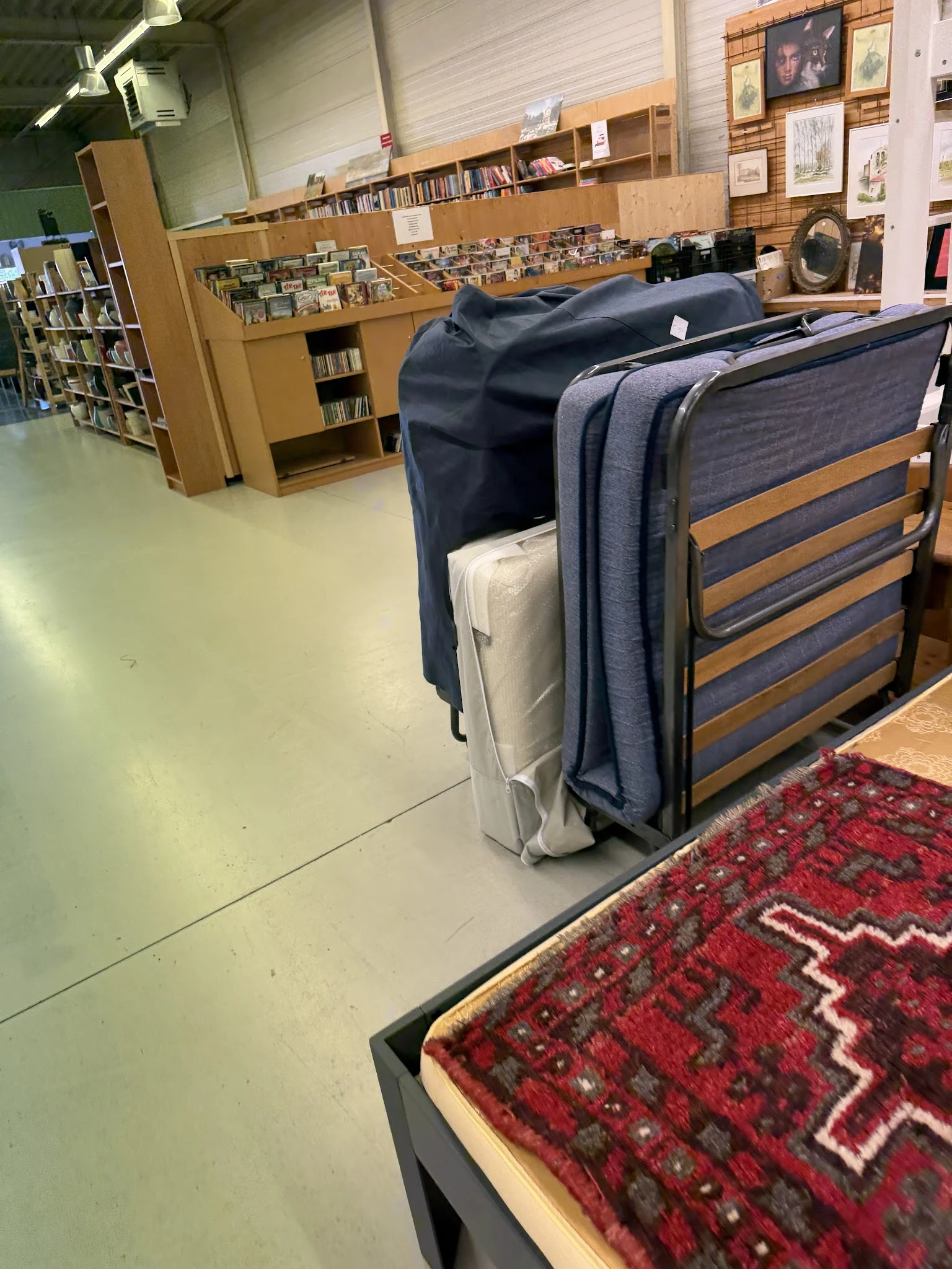 Verschillende meubels waaronder een bed en een grijze tas in een kringloopwinkel