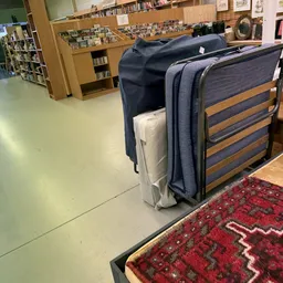 Verschillende meubels waaronder een bed en een grijze tas in een kringloopwinkel