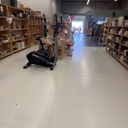 Winkelvloer van kringloopwinkel met houten stellingen vol spullen en een zwarte hometrainer in het midden