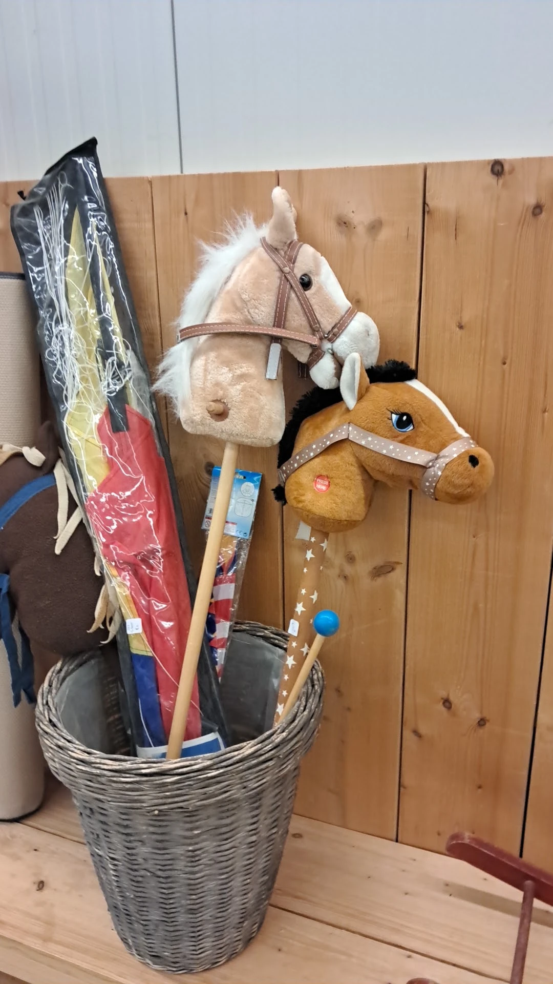 Speelgoedpaarden en kinderspeelgoed hangend aan houten wand in kringloopwinkel