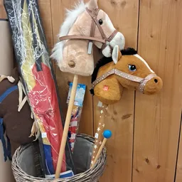 Speelgoedpaarden en kinderspeelgoed hangend aan houten wand in kringloopwinkel