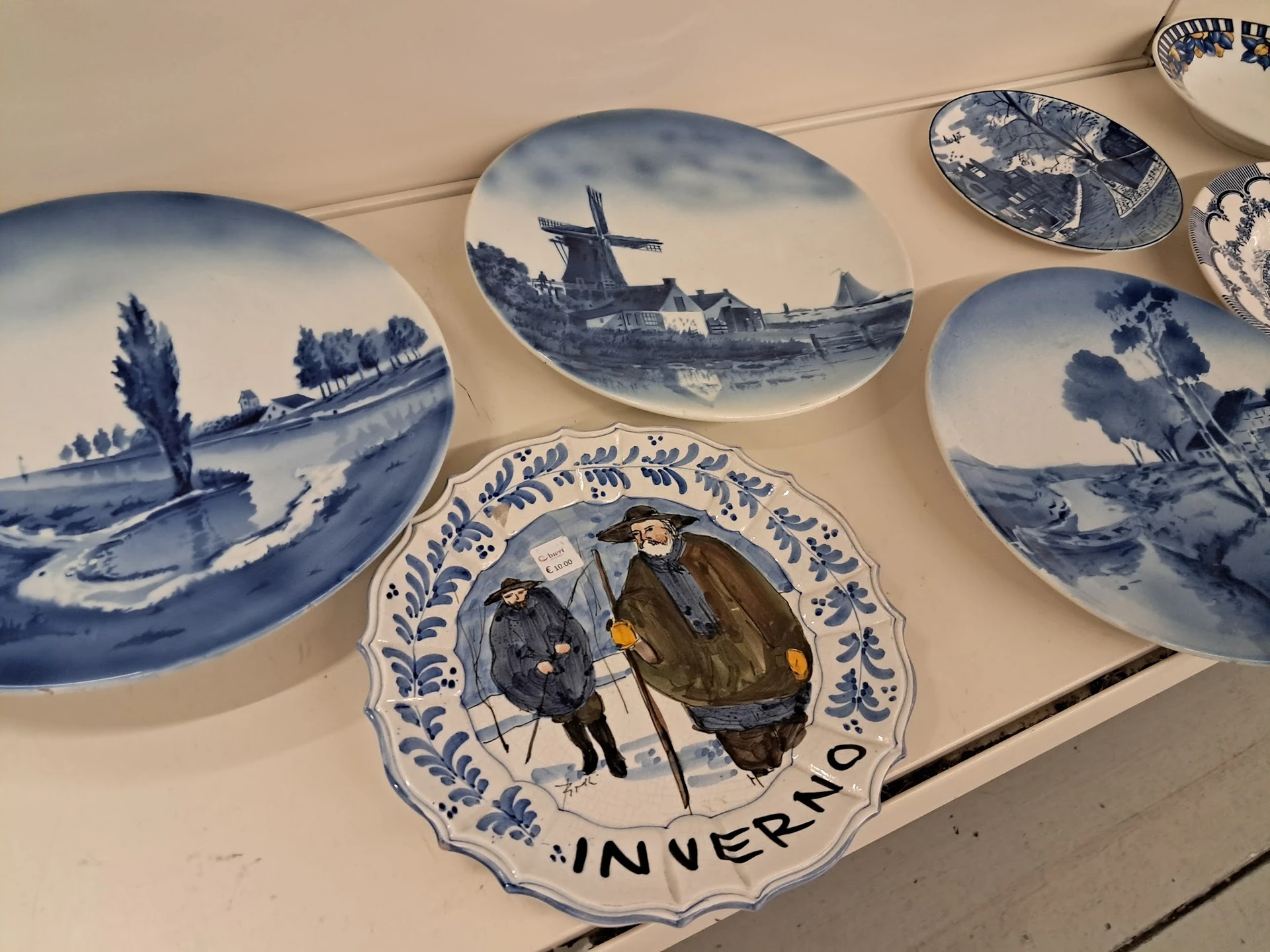 Verzameling decoratieve borden met Delfts blauw patroon, waaronder enkele met molens- en landschapsmotieven