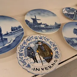Verzameling decoratieve borden met Delfts blauw patroon, waaronder enkele met molens- en landschapsmotieven