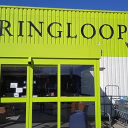 Geel-groene gevel van kringloopwinkel met grote ramen en winkeldeuren, winkelwagentjes buiten
