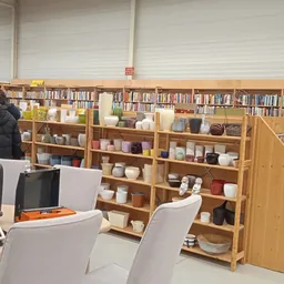 Binnenaanzicht van kringloopwinkel met houten stellingen vol boeken, serviesgoed en huishoudartikelen, laptop op tafel op voo