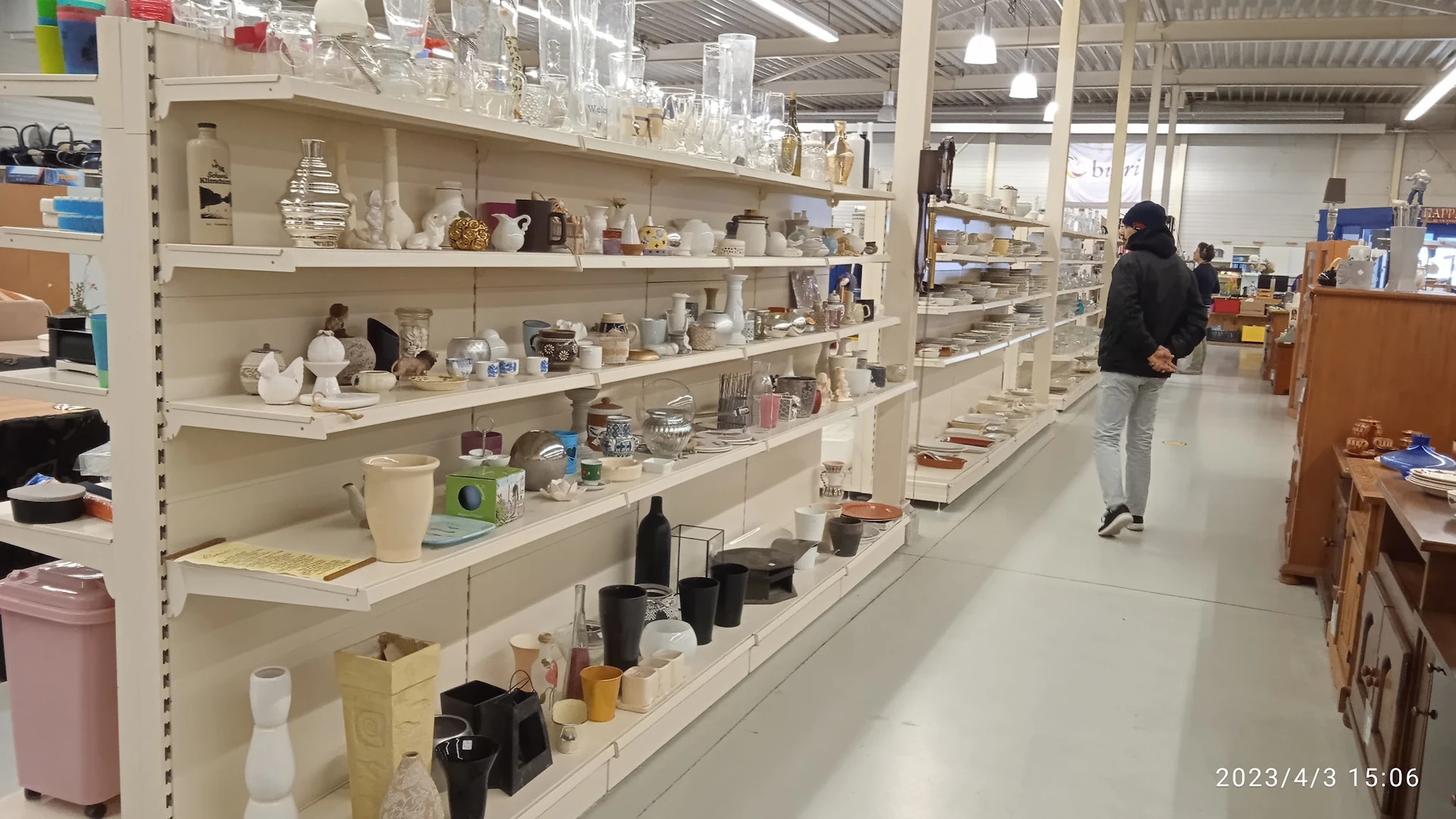 Stellingen met diverse huishoudelijke artikelen, glaswerk, flessen en decoratiespullen in een kringloopwinkel
