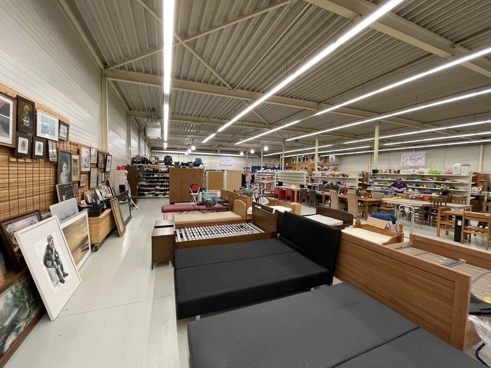 Ruim en helder magazijn/verkoopruimte met stellingen, meubels en spullen verspreid over de vloer