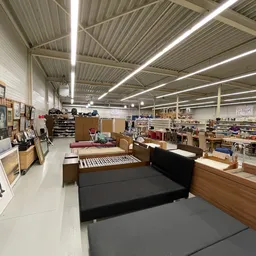 Ruim en helder magazijn/verkoopruimte met stellingen, meubels en spullen verspreid over de vloer