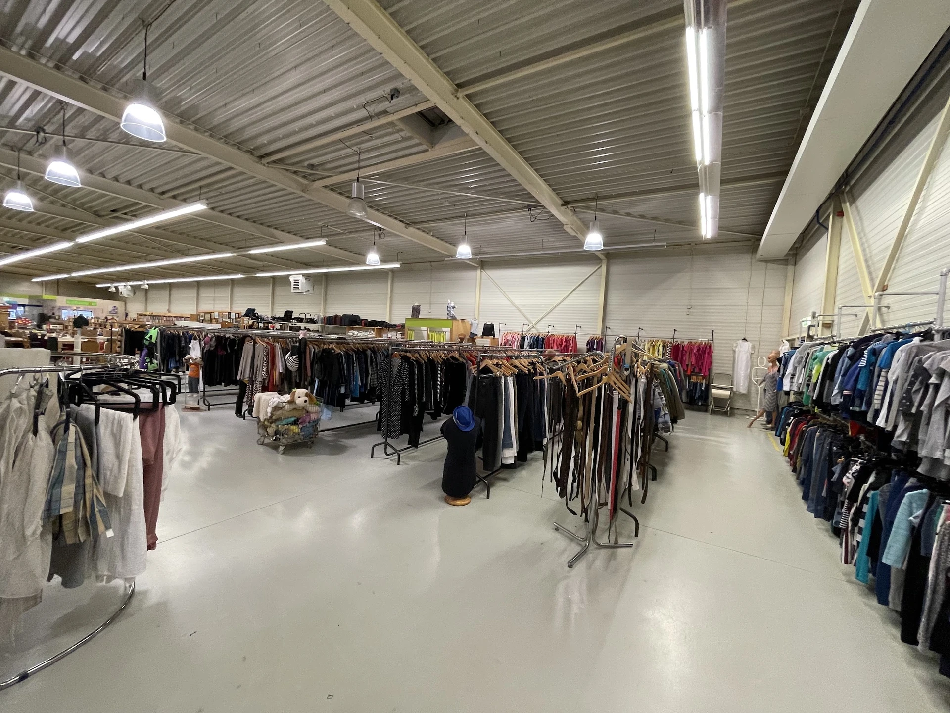 Grote hal met rekken vol tweedehands kleding, ledverlichting aan het plafond, witte vloer