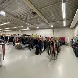 Grote hal met rekken vol tweedehands kleding, ledverlichting aan het plafond, witte vloer