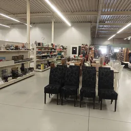 Ruim winkelinterieur met vier zwarte stoelen centraal op de vloer, stellingen met spullen aan de zijkanten en verlichting aan