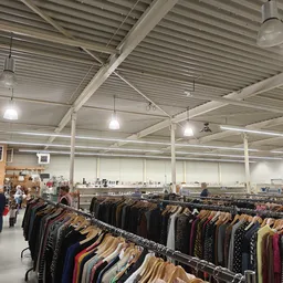 Rekken met tweedehands kleding uitgestald in een grote kringloopwinkelruimte met industrieel plafond