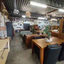 Binnenaanzicht van kringloopwinkel met meubels, tafels, stoelen en stellingen vol spullen